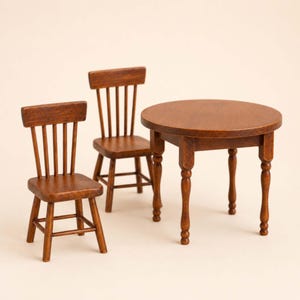 Puede incluir: Un juego de comedor de madera en miniatura con una mesa redonda y dos sillas. La mesa tiene un acabado marrón oscuro con patas torneadas. Las sillas tienen un diseño de respaldo de listones y también están acabadas con una mancha marrón oscuro. Para una casa de muñecas.