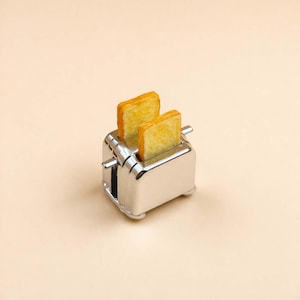 Op de afbeelding: Een glanzende, chromen broodrooster met twee sneetjes goudbruine toast. De broodrooster heeft een klassiek, retro ontwerp. De afbeelding is tegen een neutrale achtergrond geplaatst. Een keukenapparaat.