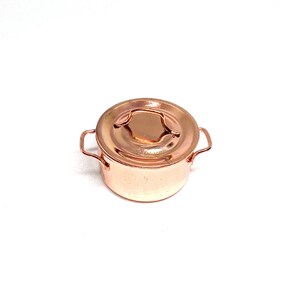 Può includere: Una pentola in miniatura color rame con un coperchio abbinato. La pentola ha due piccole maniglie e una maniglia decorativa sul coperchio. La pentola è progettata per scopi decorativi.