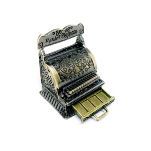 Puede incluir: Una caja registradora de metal de estilo vintage con un cajón abierto, que presenta un diseño ornamentado y la inscripción "99¢ 01¢0  Amount Purchased".
