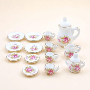 May include: A miniature porcelain tea set with a floral rose design. The set includes a teapot, creamer, sugar bowl, cups, and saucers. The pieces are white with pink and green floral accents and gold trim.