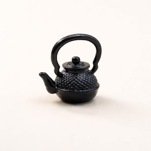Könnte beinhalten: Kleine, schwarze Teekanne mit einem Rautenmuster auf dem Körper. Sie hat einen gebogenen Griff und einen Ausguss. Der Deckel ist mit einem kleinen Knopf versehen. Die Teekanne ist ein traditionelles Design.