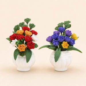 Puede incluir: Dos arreglos florales en miniatura en jarrones de cer&aacute;mica blancos. Un arreglo presenta flores rojas, amarillas y blancas con hojas verdes. El otro tiene flores moradas y amarillas con hojas verdes. Ambos jarrones tienen un dise&ntilde;o festoneado.