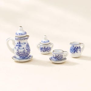 Puede incluir: Juego de té de porcelana en miniatura con diseños florales azules sobre fondo blanco. El juego incluye una tetera, azucarero, taza de té con platillo y una jarrita. La tetera tiene tapa y se apoya en un platillo pequeño.
