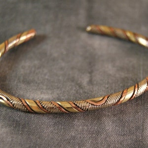 Peut inclure: Un bracelet torsadé en cuivre, laiton et argent. Le bracelet est composé de trois métaux différents qui sont entrelacés pour créer un design unique et élégant.