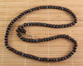 May include: A black wooden mala necklace with red, green, and white accents. The beads are round and have a smooth finish.