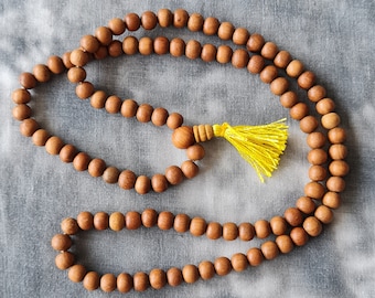 May include: A brown wooden mala bead necklace with a yellow tassel. The necklace is made of round beads and is strung on a thin cord.