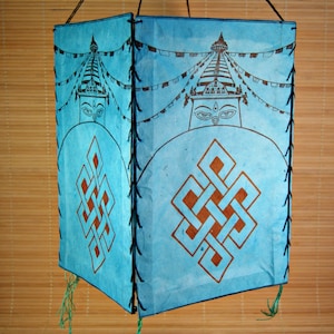 May include: A blue paper lantern with a brown and white design of a stupa with prayer flags. The lantern has a knotted design on the bottom and is hanging from a string.