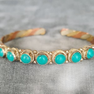 Könnte beinhalten: Ein goldfarbenes, silbernes und kupferfarbenes Armreif-Armband mit türkisfarbenen Steinen, die in Silber gefasst sind.