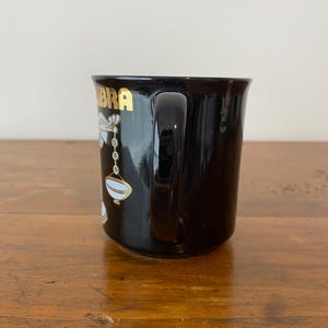 Pode incluir: Caneca de cer&acirc;mica preta com a inscri&ccedil;&atilde;o dourada "Libra" e um s&iacute;mbolo de Libra branco e dourado. A caneca tem uma al&ccedil;a curva e um acabamento brilhante. Ideal para caf&eacute; ou ch&aacute;.