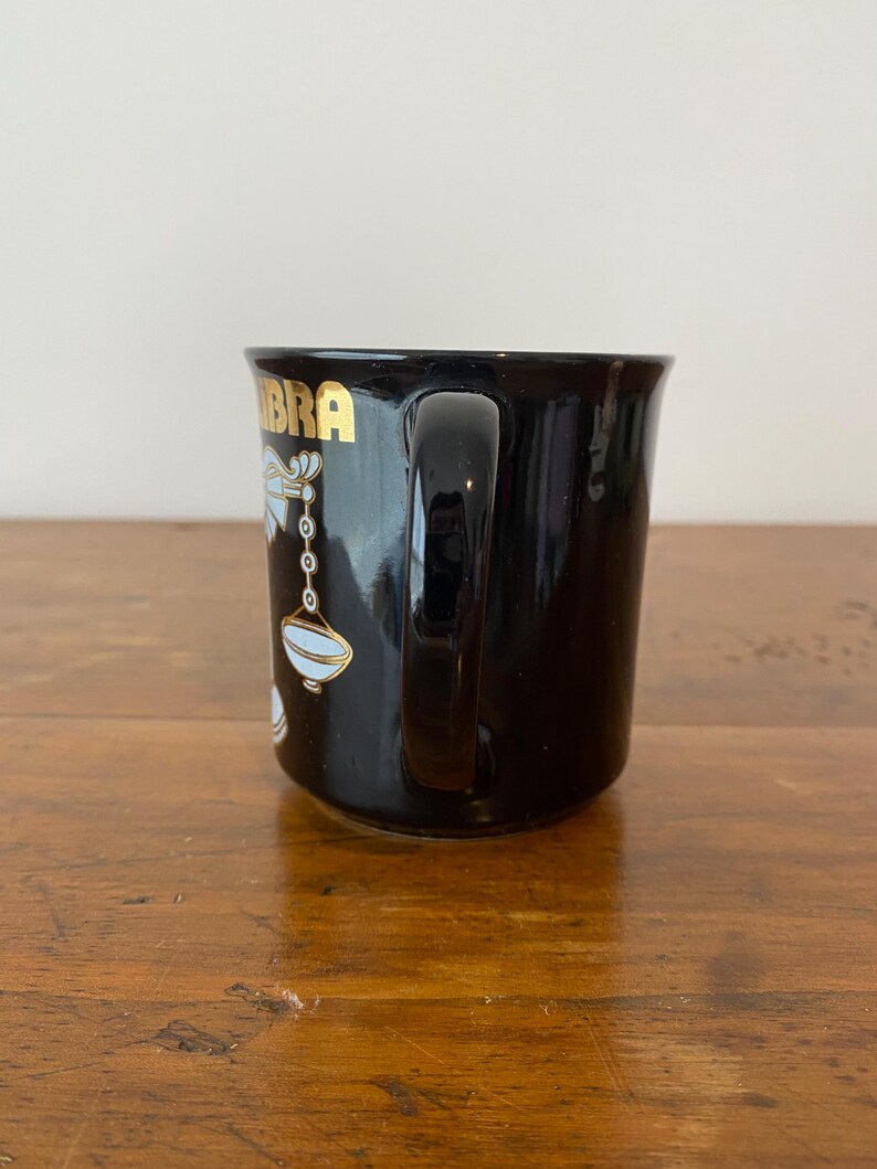 Pode incluir: Caneca de cer&acirc;mica preta com a inscri&ccedil;&atilde;o dourada "Libra" e um s&iacute;mbolo de Libra branco e dourado. A caneca tem uma al&ccedil;a curva e um acabamento brilhante. Ideal para caf&eacute; ou ch&aacute;.