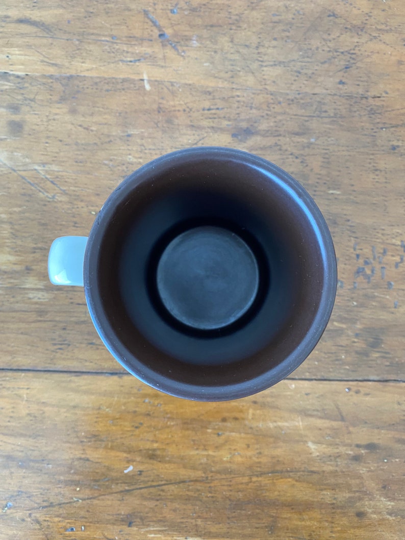 May include: A brown ceramic mug with a white handle. The mug is empty and the inside is visible.