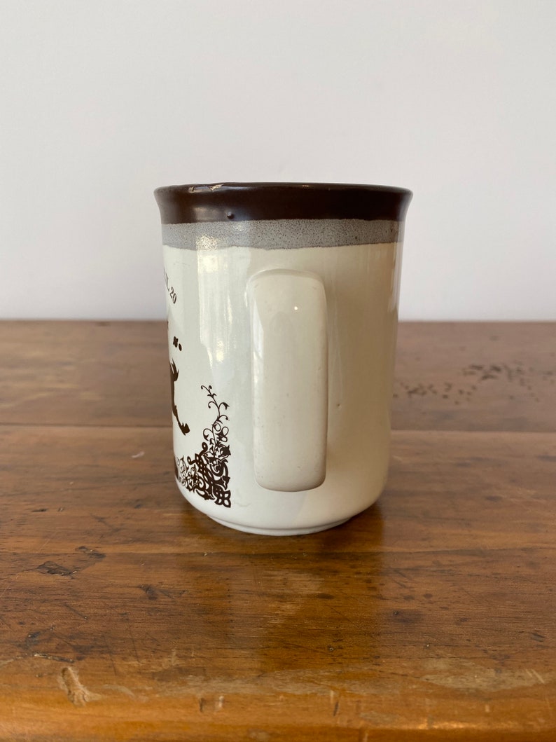 May include: A white ceramic mug with a brown rim and handle. The mug has a brown floral design on the side.