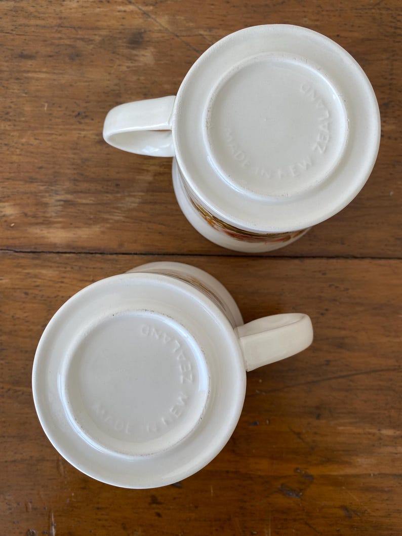 May include: Two white ceramic mugs with a floral design. The bottom of each mug reads "Made in New Zealand".
