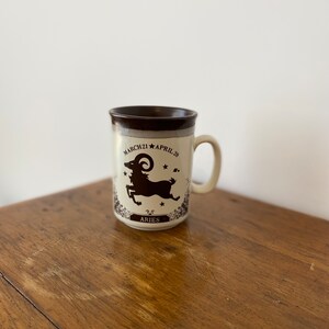 May include: A brown and white ceramic mug with a black silhouette of an Aries zodiac sign and the text "MARCH 21 APRIL 20" and "ARIES".
