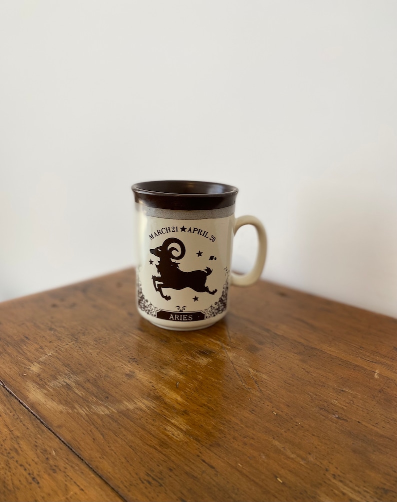 May include: A brown and white ceramic mug with a black silhouette of an Aries zodiac sign and the text "MARCH 21 APRIL 20" and "ARIES".