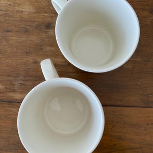 May include: Two white ceramic mugs with handles. The mugs are empty and have a smooth, glossy finish.