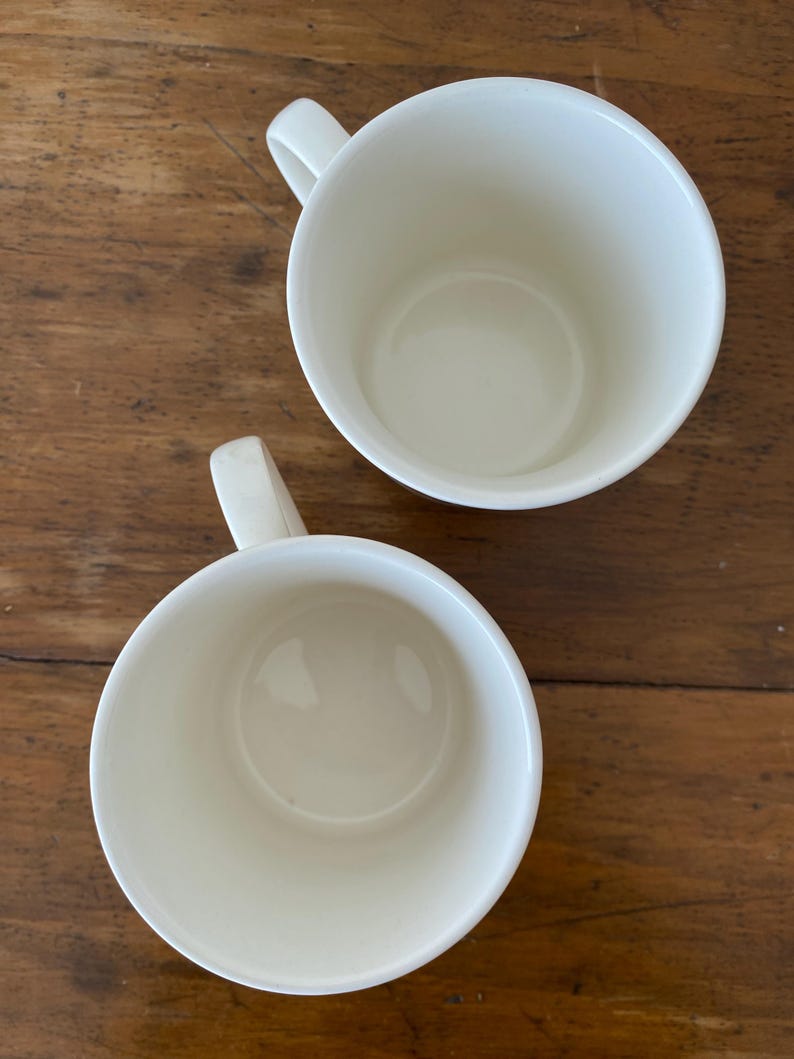 May include: Two white ceramic mugs with handles. The mugs are empty and have a smooth, glossy finish.