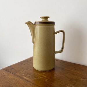 May include: A tall, light green ceramic coffee pot with a brown stripe around the top and a lid. The pot has a spout and a handle.