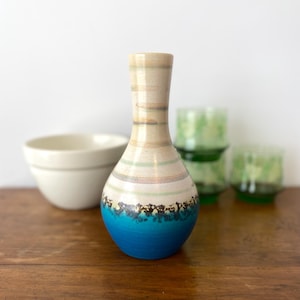 Peut inclure: Un vase en céramique décoratif avec une base bleue et un col beige. Le vase présente des rayures horizontales de différentes couleurs, dont le rose, le vert et le marron. Un bol blanc et des verres verts sont à l'arrière-plan.