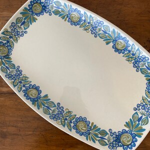 Pode incluir: Uma travessa oval branca com um design floral azul e verde ao redor da borda.