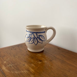 May include: A white ceramic mug with a blue floral design. The mug has a rounded body and a handle.