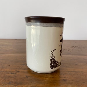 May include: A white ceramic mug with a brown rim and a brown design of a horse and floral pattern. The mug says "Magic" on the side.