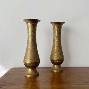 Pode incluir: Dois vasos de metal dourado com um design floral ornamentado. Os vasos são altos e finos com uma base redonda.