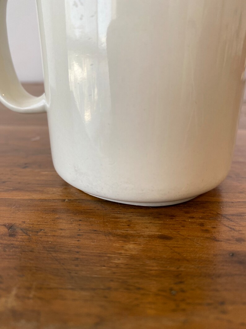 May include: A white ceramic mug with a handle. The mug is sitting on a wooden surface.