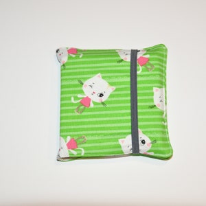 Könnte beinhalten: Grüne Stofftasche mit einem weißen Katzenmotiv und einem schwarzen Gummizug. Die Katze trägt ein rosa Kleid und hat ein weißes Gesicht mit schwarzen Augen.