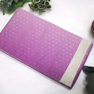 May include: A rectangular fabric item featuring a vibrant purple section with a repeating white geometric star pattern and a contrasting solid light beige panel on one side. The fabric has a smooth texture and is folded into a flat, clean shape.