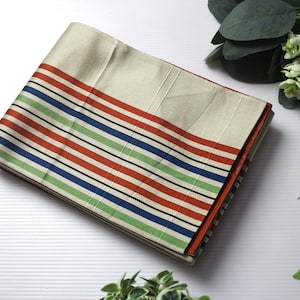 May include: Folded cream-colored fabric with a striped border in red, green, blue, and black. The fabric is neatly stacked, showcasing a clean and organized appearance. The design is simple and elegant.
