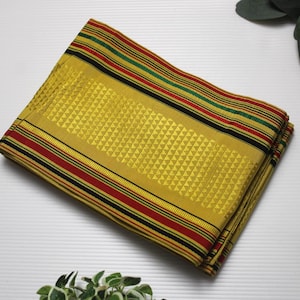 Puede incluir: Tela amarilla doblada con un patrón geométrico y bordes a rayas en rojo, negro y verde. La tela está cuidadosamente apilada, mostrando su diseño y textura. El tema general es textil y diseño.