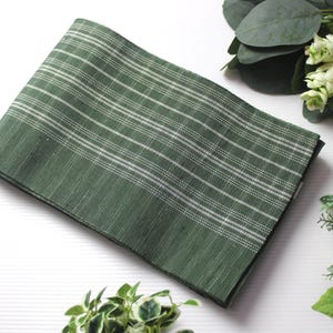 May include: A folded green textile with white horizontal stripes. The fabric is surrounded by greenery and a decorative ball with red and black accents. The textile is likely a decorative cloth or a kitchen towel.