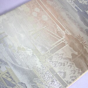 May include: A detailed close-up of a textile with a Japanese-inspired design. The fabric features a landscape with architectural elements, trees, and floral patterns in shades of gray, beige, and pale pink. The design is intricate and detailed.