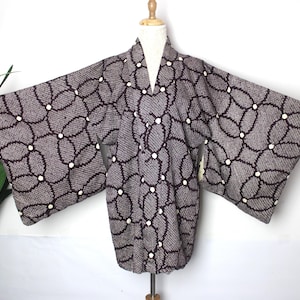 Może przedstawiać: Ciemnoszare kimono z powtarzającym się wzorem połączonych owali i białych kropek. Kimono ma szerokie rękawy i kołnierz w kształcie litery V. Ubranie jest prezentowane na manekinie.