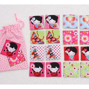 Könnte beinhalten: Ein Set aus 12 bunten Stoffquadraten mit verschiedenen Designs, darunter Schmetterlinge, Blumen und japanische Puppen. Die Quadrate befinden sich in einem rosa Kordelbeutel.