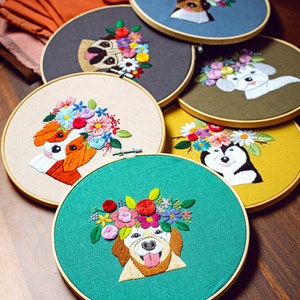 Pode incluir: Seis aros de bordado com tecidos de diferentes cores e imagens bordadas de cães com coroas de flores. Os cães são um pug, um spaniel, um husky e um golden retriever.