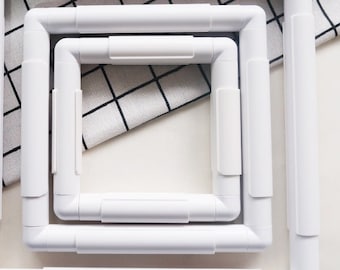 May include: Three white plastic embroidery hoops of different sizes. The hoops are nested inside each other.