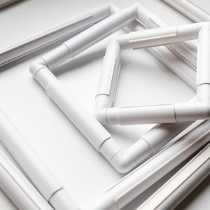 May include: Four white plastic embroidery hoops of different sizes, stacked on top of each other. The hoops are designed to hold fabric taut while stitching.