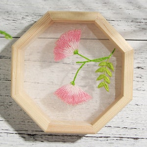 Peut inclure: Un cadre octogonal en bois avec un motif de fleur brod&eacute;e rose et verte. La broderie est sur un fond de tissu blanc.