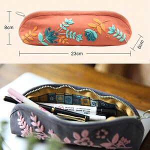 May include: A gray and orange pencil case with floral embroidery. The case is 23 cm long, 8 cm tall, and 6 cm wide. The case is open to reveal a yellow and blue patterned lining.