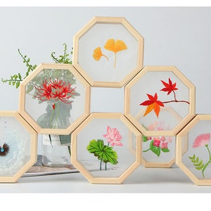 Peut inclure: Ensemble de huit cadres octogonaux en bois avec des motifs floraux brod&eacute;s. Les cadres sont dispos&eacute;s en forme de nid d'abeille et pr&eacute;sentent diverses fleurs, notamment des lys araign&eacute;es rouges, des lotus roses et des fleurs blanches avec des centres bleus.