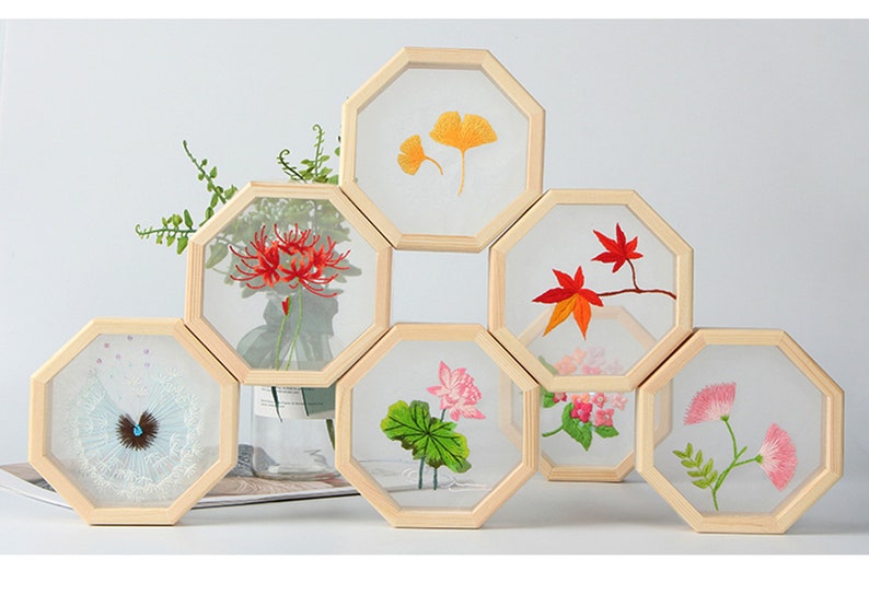 Peut inclure: Ensemble de huit cadres octogonaux en bois avec des motifs floraux brod&eacute;s. Les cadres sont dispos&eacute;s en forme de nid d'abeille et pr&eacute;sentent diverses fleurs, notamment des lys araign&eacute;es rouges, des lotus roses et des fleurs blanches avec des centres bleus.