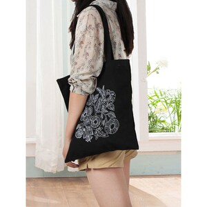 May include: A black tote bag with a white floral design. The bag has a long strap and is made of canvas.