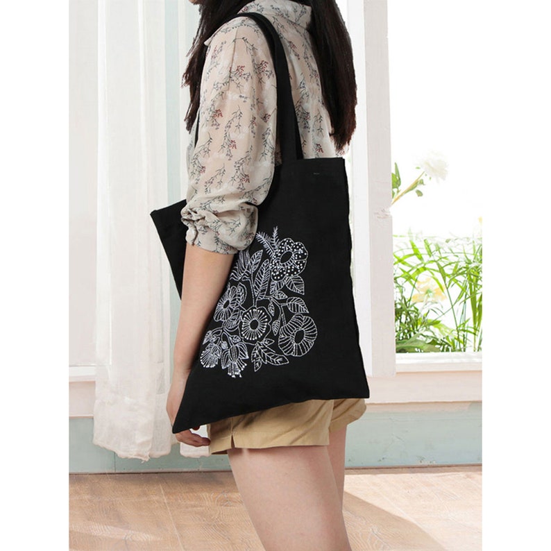 May include: A black tote bag with a white floral design. The bag has a long strap and is made of canvas.