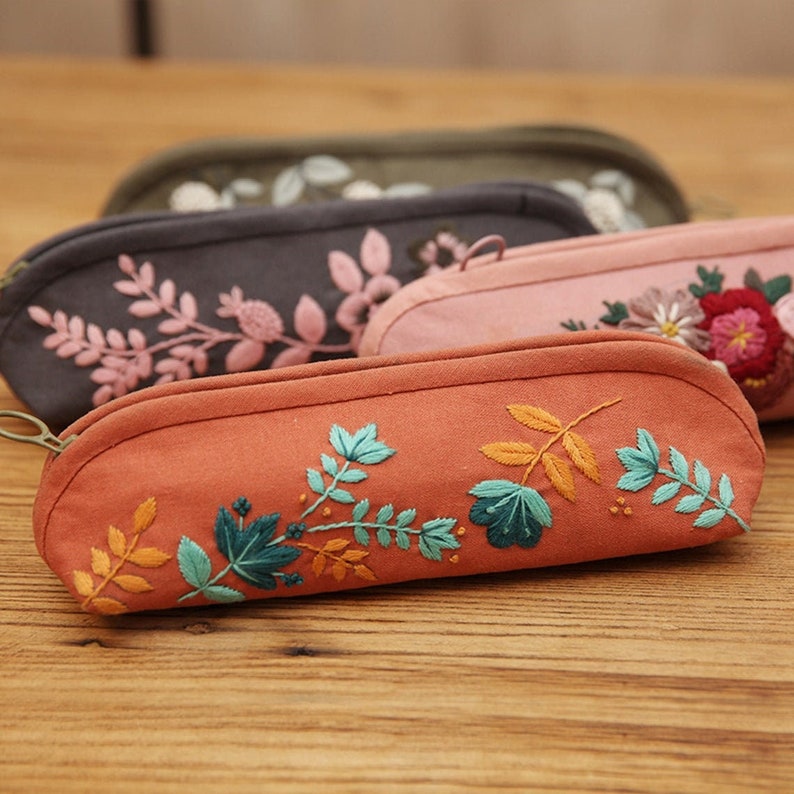 May include: Four embroidered zippered pouches in different colors. The pouches are made of a soft, textured fabric and feature floral embroidery in shades of pink, green, and orange.