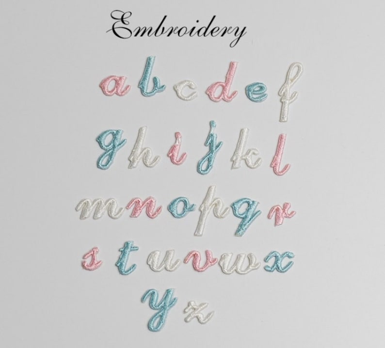 May include: Embroidered alphabet letters in white, pink, and light blue. The letters are in a cursive font and are arranged in rows.
