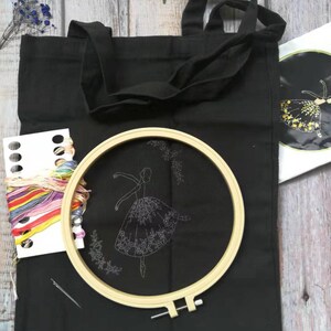 May include: A black tote bag with a white embroidery design of a ballerina in a flowing skirt. The bag comes with a hoop, embroidery floss, and a needle.