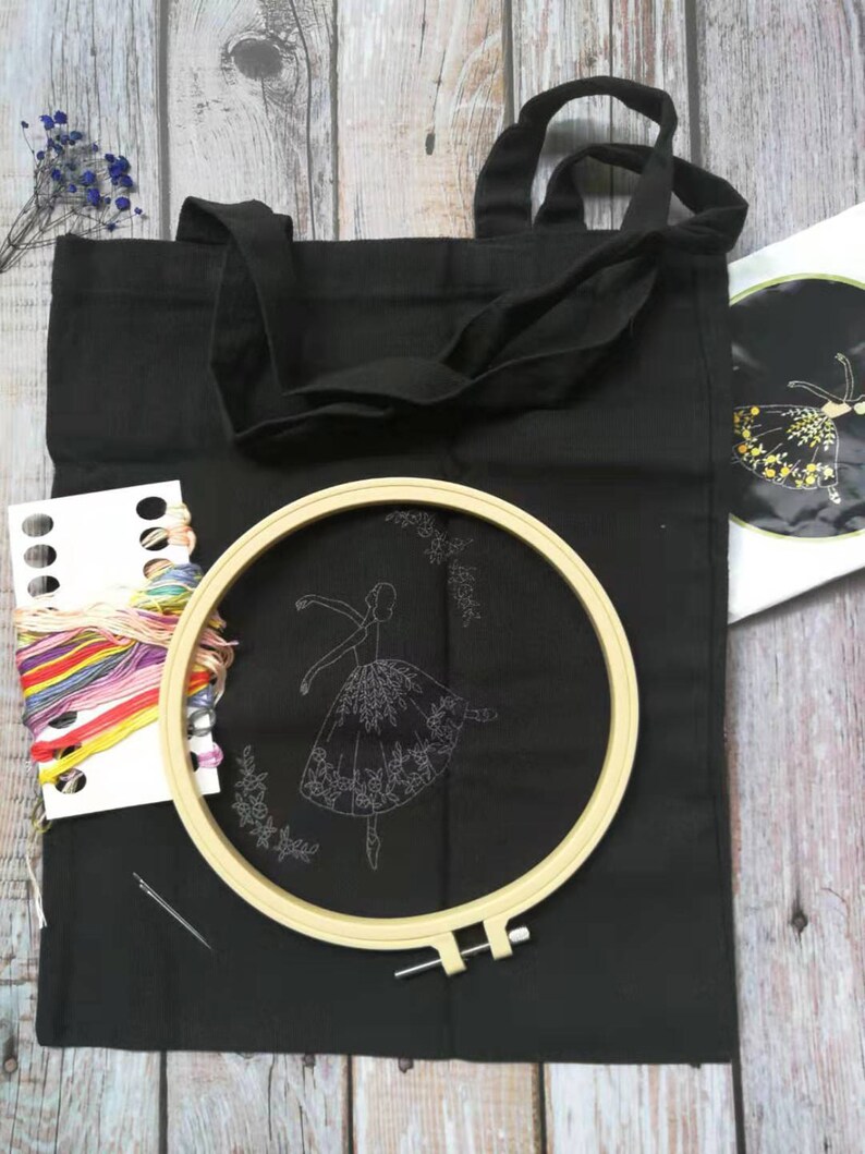 May include: A black tote bag with a white embroidery design of a ballerina in a flowing skirt. The bag comes with a hoop, embroidery floss, and a needle.